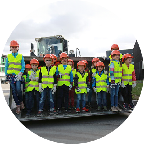 Kindergruppe während Führung mit Warnwesten und Helmen in Radladerschaufel