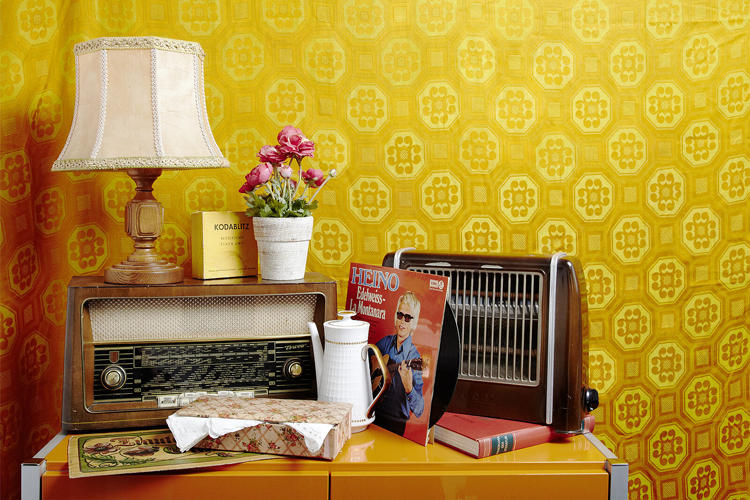 Retro Einrichtung mit alter Lampe und altem Radio sowie Blumen, Schallplatte und weiterer Dekoration vor einer gelben Tapete 